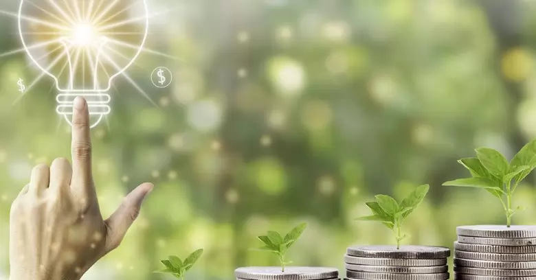 imagem representativa de uma lâmpada e moedas com a natureza ao fundo traz a analogia de economia de energia na empresa