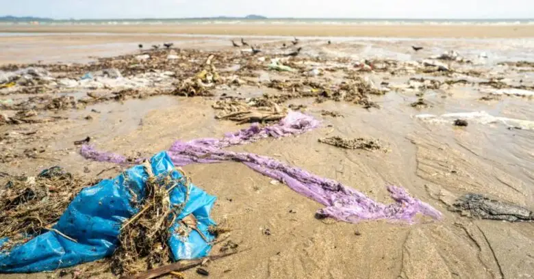 Lixo e tecidos acumulados na areia de uma praia exemplificam os impactos ambientais da moda.